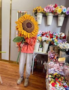 a person holding a large sunflower in front of a flower shop filled with flowers