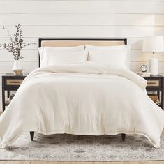 a bed with white linens and pillows in a room next to a lamp on a table