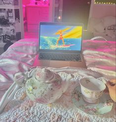 a laptop computer sitting on top of a bed next to two cups and saucers