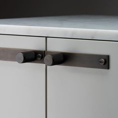 two metal handles on the front of a white cabinet