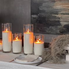 four candles are lit on a table in front of a painting and place setting with silverware