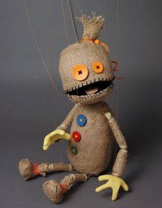 an odd looking stuffed animal with orange eyes and yellow hands, holding strings attached to it's head