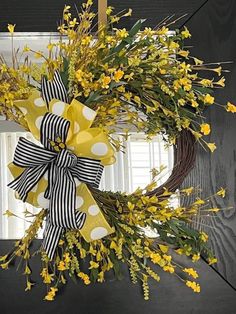 a wreath with yellow flowers and black and white ribbon hanging from the front door,