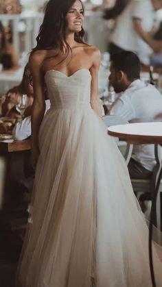 a woman in a wedding dress standing next to a table with people sitting at tables