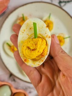 a hand holding an egg shell with deviled eggs in the background