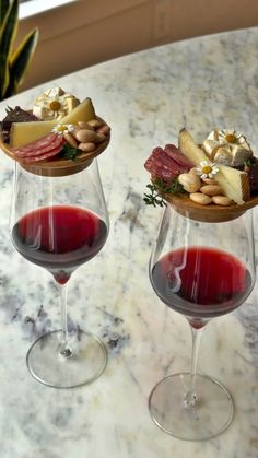 two wine glasses filled with different types of food on top of a marble countertop