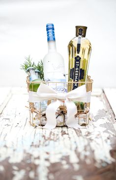 two bottles of alcohol are sitting in a basket with a bow on the table next to it