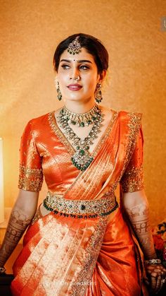 a woman in an orange and gold sari standing next to a table with flowers