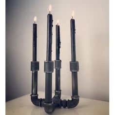 three black candles sitting next to each other on top of a white table with one burning