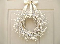 a wreath is hanging on the front door with white flowers and pearls attached to it