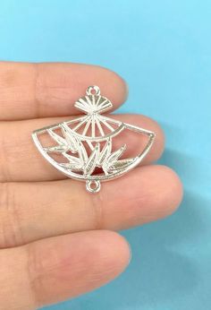 a hand holding a silver brooch with leaves on it's back and bottom