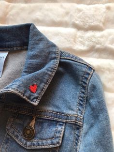 a denim jacket with a red heart on the front and back buttons, sitting on a bed