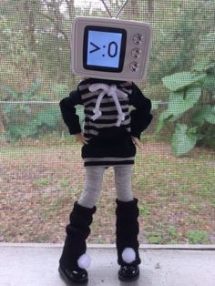 a doll with a clock on its head standing in front of a mesh screen window