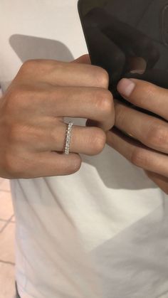 a person holding a cell phone and wearing a diamond ring on their left hand, in front of a white t - shirt