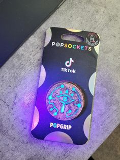 a purple and blue sticker on top of a black box with the word pop sockets printed on it