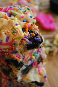 a stack of cookies covered in sprinkles and colored frosting on top of a wooden table