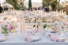 an outdoor wedding reception with pink and white flowers on the table, candles in vases