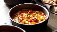 two bowls filled with chili and meat on top of a metal table next to bread