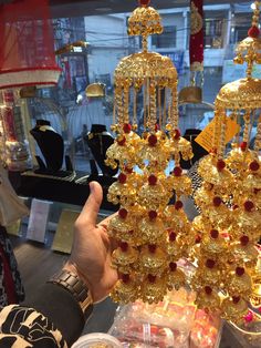 a person holding up some gold jewelry in front of a store display case with other items on it