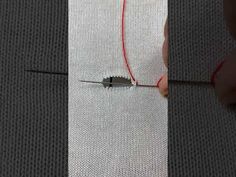 someone is working on something that looks like a piece of fabric with red thread in it