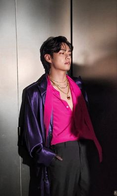 a man in a pink shirt and black pants standing next to a metal wall with his hands on his hips