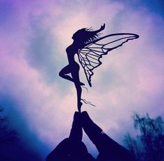 two hands holding up a silhouette of a fairy on a purple sky with trees in the background