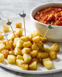 a white plate topped with food next to a bowl of sauce and toothpicks