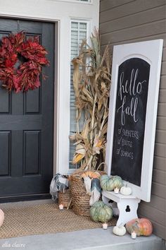 a front porch decorated for fall with pumpkins, gourds and a chalkboard sign