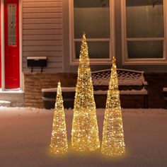 three lighted christmas trees in front of a house