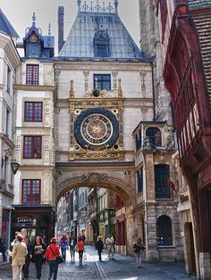 people are walking down an alley way with buildings and a clock on the building's side