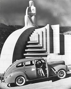 an old car parked in front of a building with a woman standing on the stairs