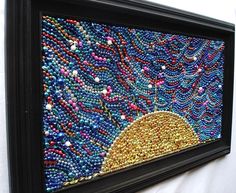 beaded artwork displayed in black frame on white tablecloth with red, yellow and blue beads