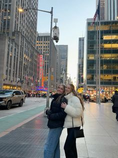 two people standing next to each other in front of tall buildings on a city street