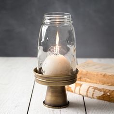 a candle in a glass jar on a wooden table next to an old book and wood block