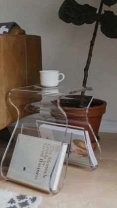 there is a glass table with books and a cup on it next to a potted plant