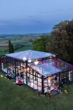 an aerial view of a glass house in the middle of a green field at night