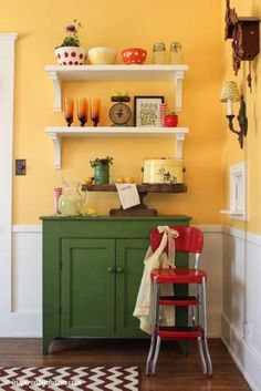 a kitchen with yellow walls and green cabinetry, red chair in the foreground