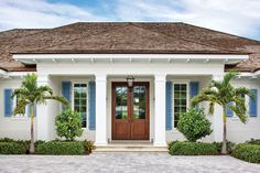 a white house with blue shutters and palm trees in front of the entrance door