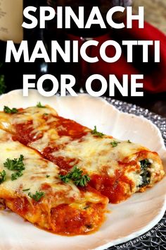 two slices of spinach manicotti on a plate next to a bottle of wine