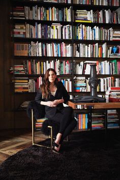 a woman sitting on a chair in front of a bookshelf filled with books