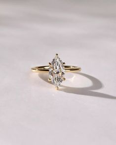 a yellow gold ring with a pear shaped diamond in the center on a white surface