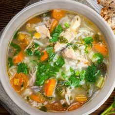 a white bowl filled with chicken and vegetable soup next to some bread on a table