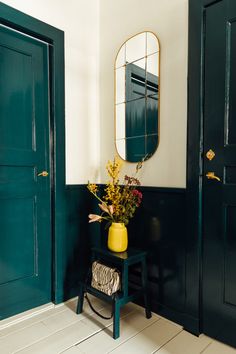 a room with green doors and a yellow vase on a small table in front of it