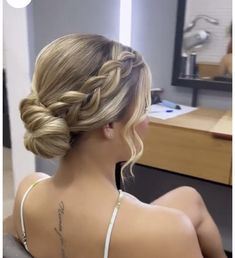 a woman sitting in front of a mirror with her back to the camera and braided hair