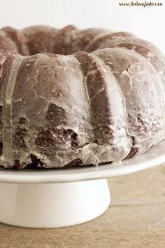 a bundt cake sitting on top of a white cake plate covered in frosting