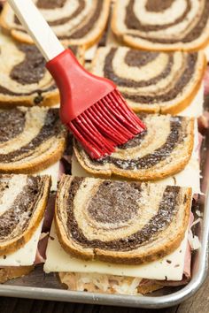 a red brush is sticking out of some cinnamon roll sandwiches on a baking sheet with other pastries in the background