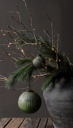 a green ball hanging from a tree branch with christmas lights in the back ground and behind it is an ornament