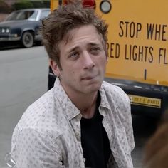 a man sitting in front of a school bus on the street with traffic behind him