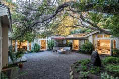 the back yard is surrounded by large trees and gravel, with seating areas on either side