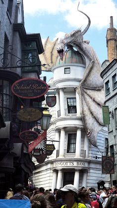 a large white dragon statue on the side of a building with lots of people around it